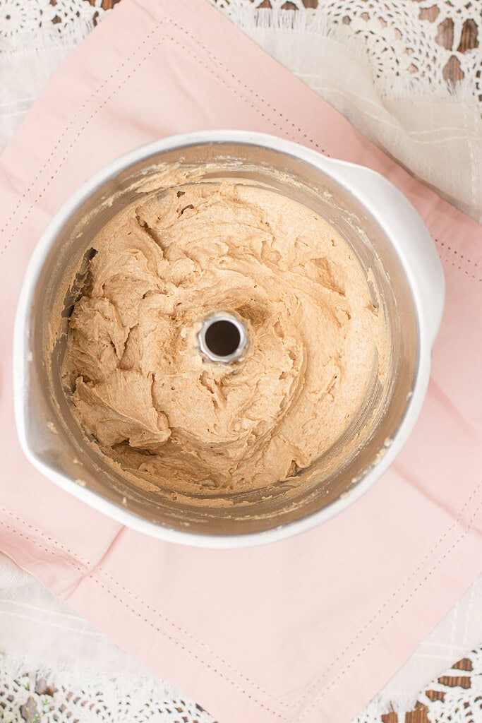 Overhead view of creamed butter and sugar cookie dough in a stand mixer bowl, smooth and fluffy, on a pink linen napkin with crochet lace.