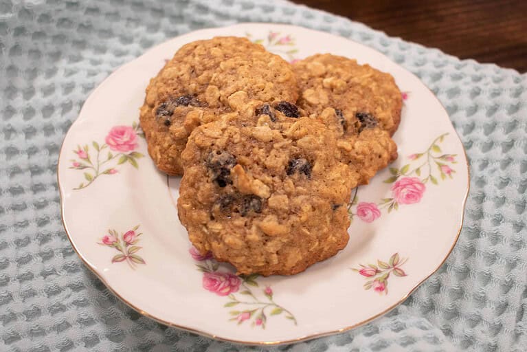 three sourdough einkorn oatmeal raisin cookies on a pink floral china plate on a sage green dish towel on a wooden countertop