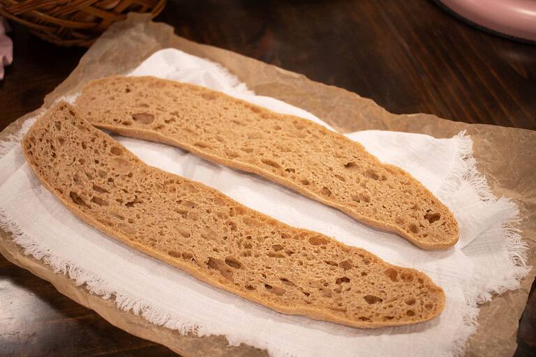 a open sliced Artisan Sourdough Baguette on a creme kitchen cloth on a crinkled piece of parchment paper
