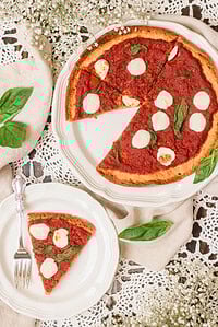 Whole sourdough discard pizza with one slice removed, topped with tomato sauce, mozzarella rounds, and fresh basil on a white serving plate.