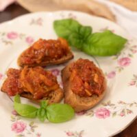 Three pieces of homemade bruschetta on a pink floral plate in a cottage kitchen.