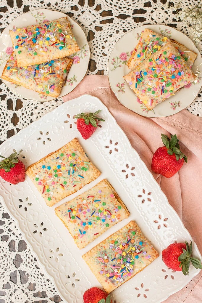 Assorted homemade sourdough discard pop-tarts with glaze and sprinkles arranged on plates with fresh strawberries.