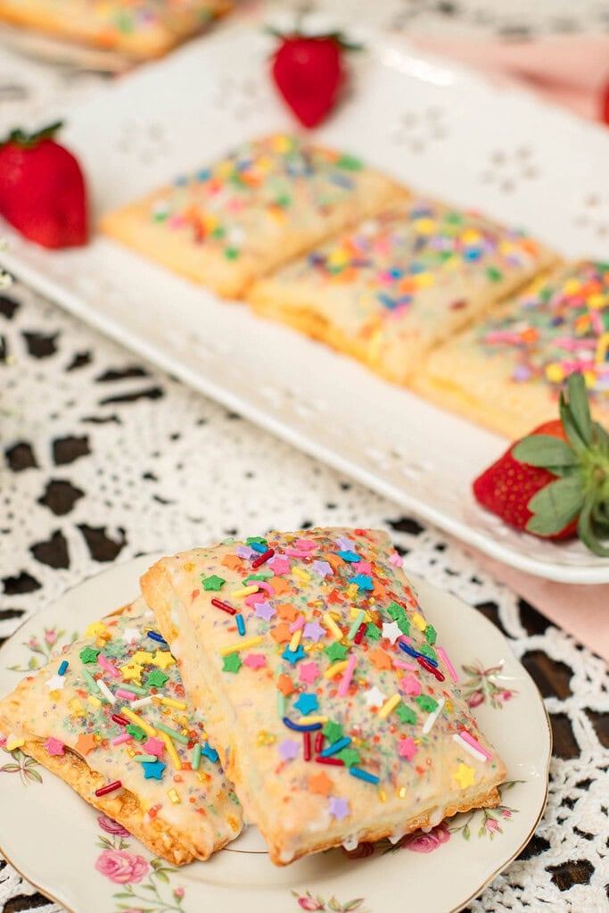 Homemade sourdough discard pop-tarts filled with jam and topped with glaze and sprinkles on a floral plate.