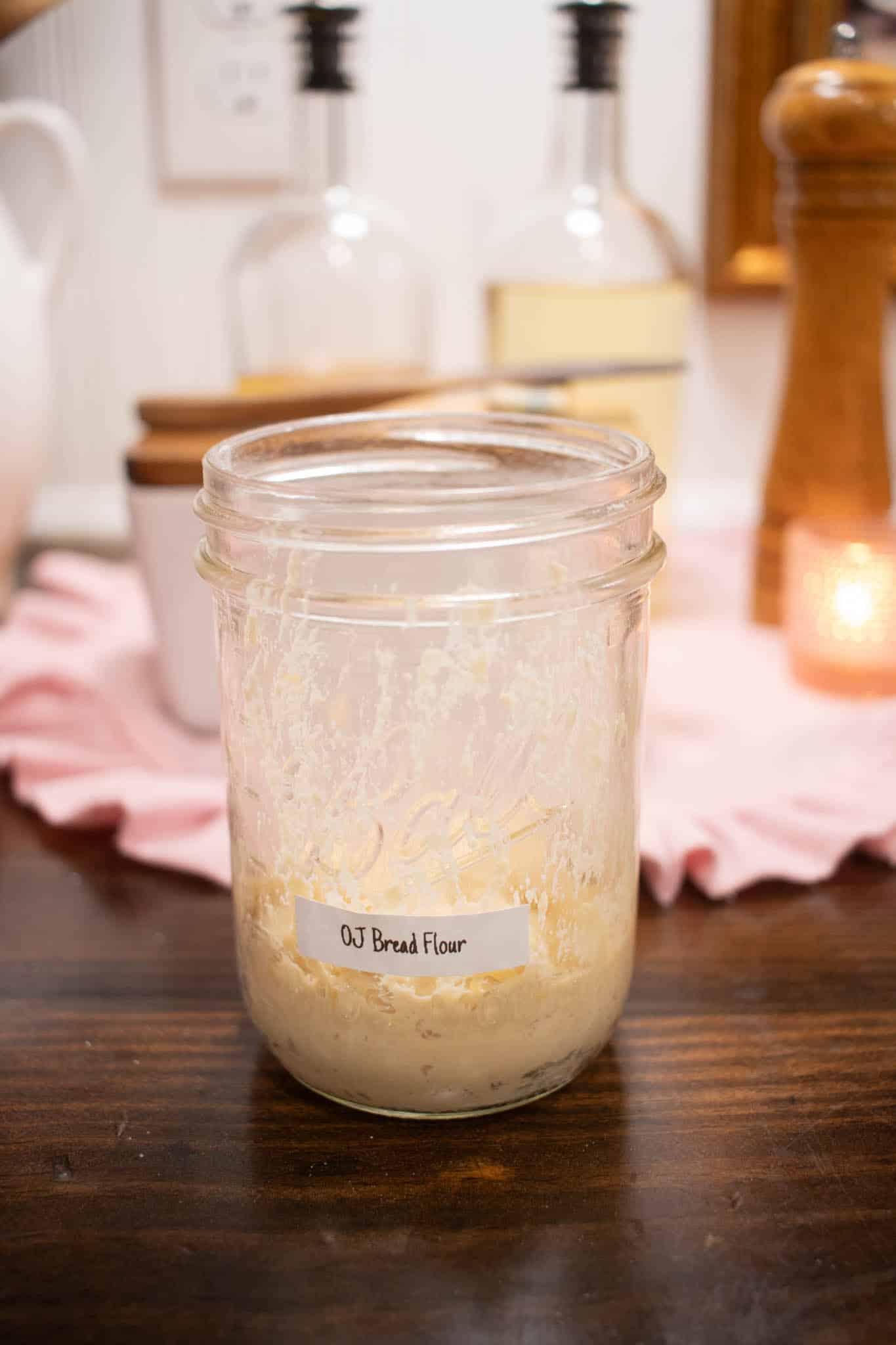 a pint sized mason jar filled with bread flour sourdough starter on a wooden countertop in a cottage kitchen