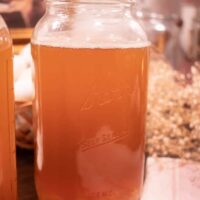 a half gallon sized mason jar filled with water kefir and white babys breath in the background in a cosy cottage kitchen