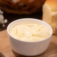 a white small bowl of mayonnaise on a wooden cutting board in a cottage kitchen