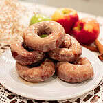 A plate of glazed sourdough apple cider doughnuts stacked, with fresh apples and cinnamon sticks around for a cozy fall vibe.