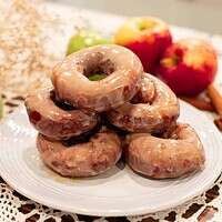 A plate of glazed sourdough apple cider doughnuts stacked, with fresh apples and cinnamon sticks around for a cozy fall vibe.