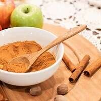 A bowl of homemade apple pie spice surrounded by fresh red and green apples, cinnamon sticks, and nutmeg on a wooden board, perfect for fall baking.