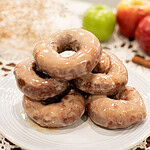 Stack of glazed sourdough apple cider donuts on a white plate with apples in the background