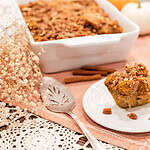 A slice of sourdough pumpkin French toast casserole on a plate with cinnamon sticks and a casserole dish in the background, accompanied by autumn decor.