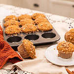 A display of sourdough pumpkin spice muffins, with a couple placed on a plate, showcasing their golden color and streusel topping, surrounded by mini pumpkins and a muffin tin full of more muffins.