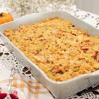 A close-up of the baked sourdough cornbread dressing in a ceramic baking dish, with a spoon ready to serve. The dish’s golden-brown texture captures the rustic appeal of a comforting holiday side dish.