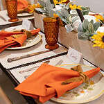 A detailed view of a fall table setting with a sunflower-decorated plate, orange napkin tied with a mustard ribbon, amber goblet, and a centerpiece of pumpkins, lamb’s ear greenery, and sunflowers.