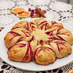 A side view of the cranberry orange star bread, showing the soft, fluffy texture and vibrant cranberry filling. The table setting includes crocheted lace and festive garnishes like dried oranges and cranberries.