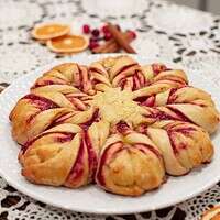 A side view of the cranberry orange star bread, showing the soft, fluffy texture and vibrant cranberry filling. The table setting includes crocheted lace and festive garnishes like dried oranges and cranberries.