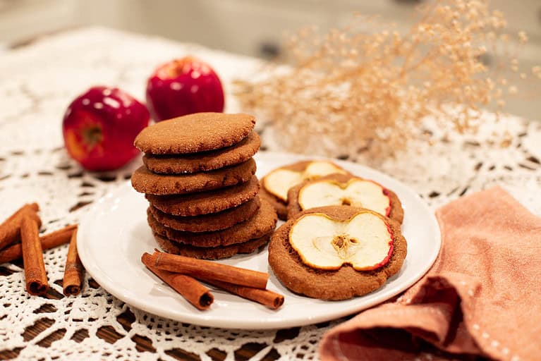Close-up of a plate of Sourdough Nutmeg Ginger Apple Snaps, featuring a mix of plain cookies and cookies topped with apple slices.