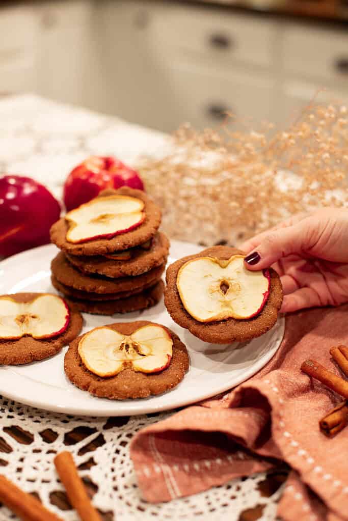 A hand holding a Sourdough Nutmeg Ginger Apple Snap with an apple slice on top, showcasing the rustic and cozy look of the finished cookie.