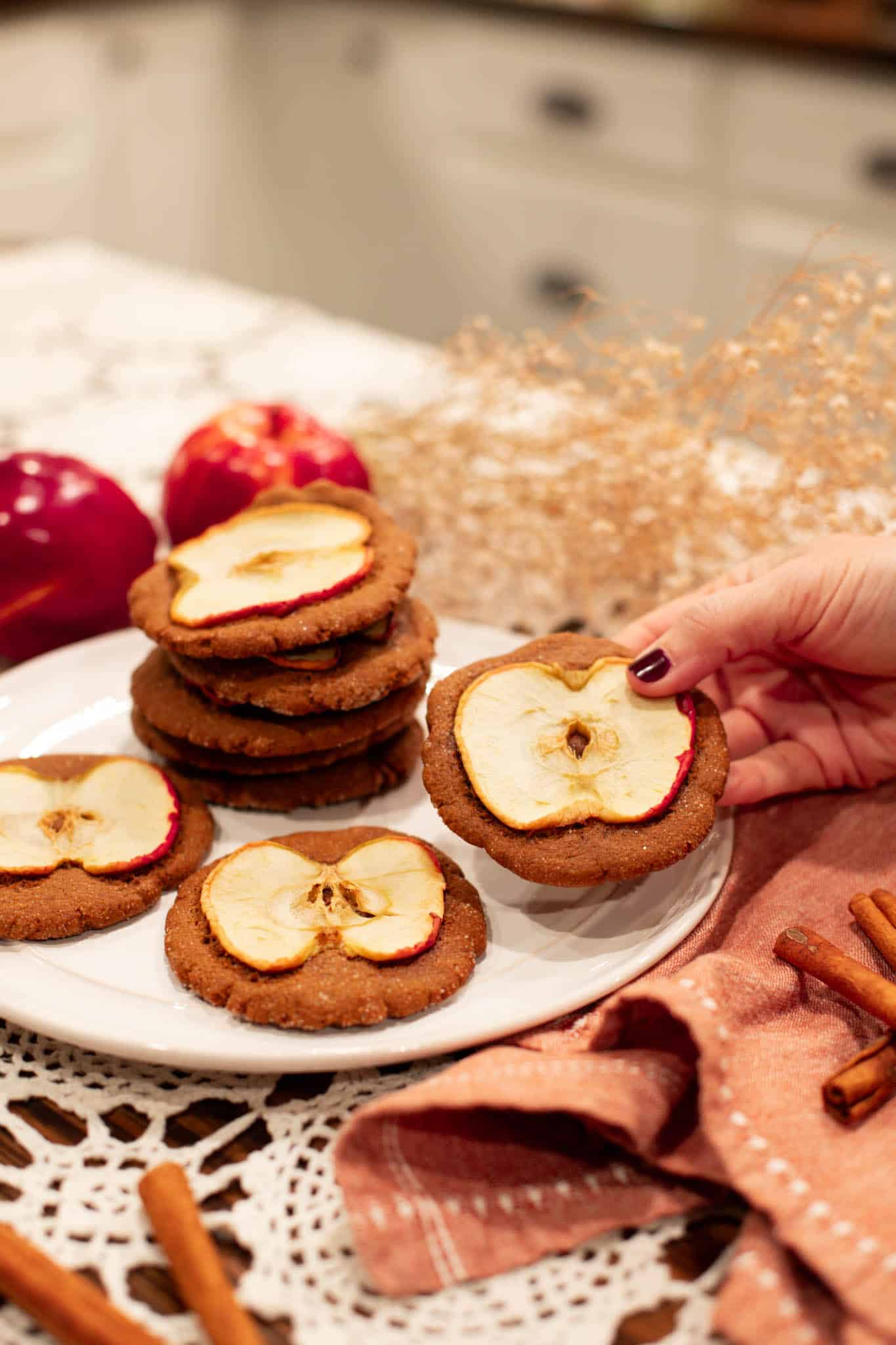 A hand holding a Sourdough Nutmeg Ginger Apple Snap with an apple slice on top, showcasing the rustic and cozy look of the finished cookie.