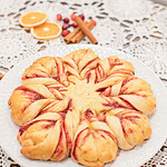 A sourdough cranberry orange star bread on a white plate showing the golden twisted star shape with deep red cranberry filling, styled on a lace doily with dried orange slices, fresh cranberries, and cinnamon sticks in a cottage kitchen.
