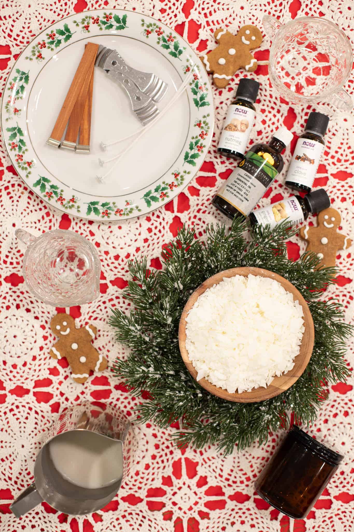 A cozy holiday setup featuring a bowl of melted soy wax, candle wicks, and greenery, showcasing the preparation process for Christmas-themed candles.