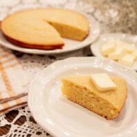 A slice of golden sourdough discard cornbread with butter melting on top, served on a white plate with a cozy backdrop.