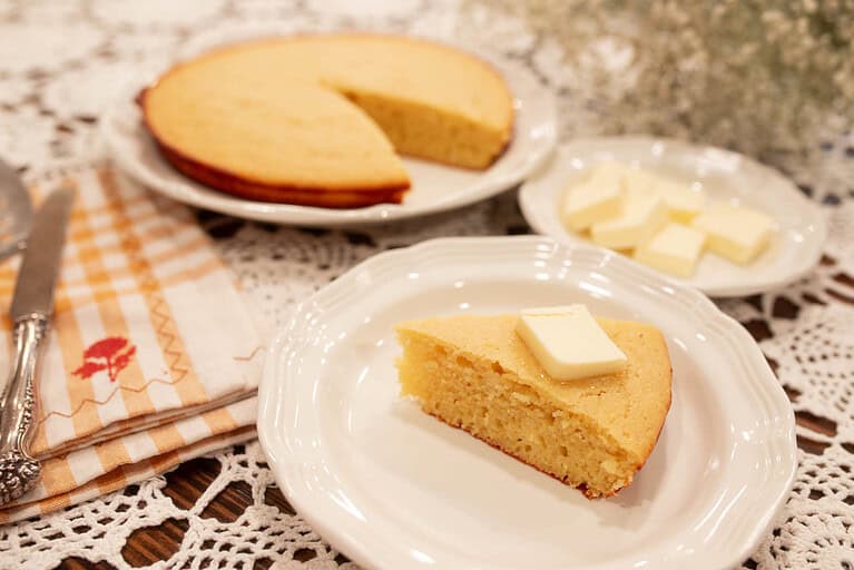 A slice of golden sourdough discard cornbread with butter melting on top, served on a white plate with a cozy backdrop.