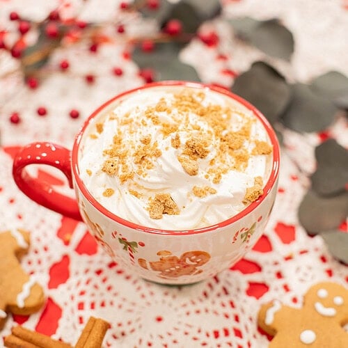 homemade gingerbread latte with whipped cream and crushed cookies in holiday mug on cozy winter setting