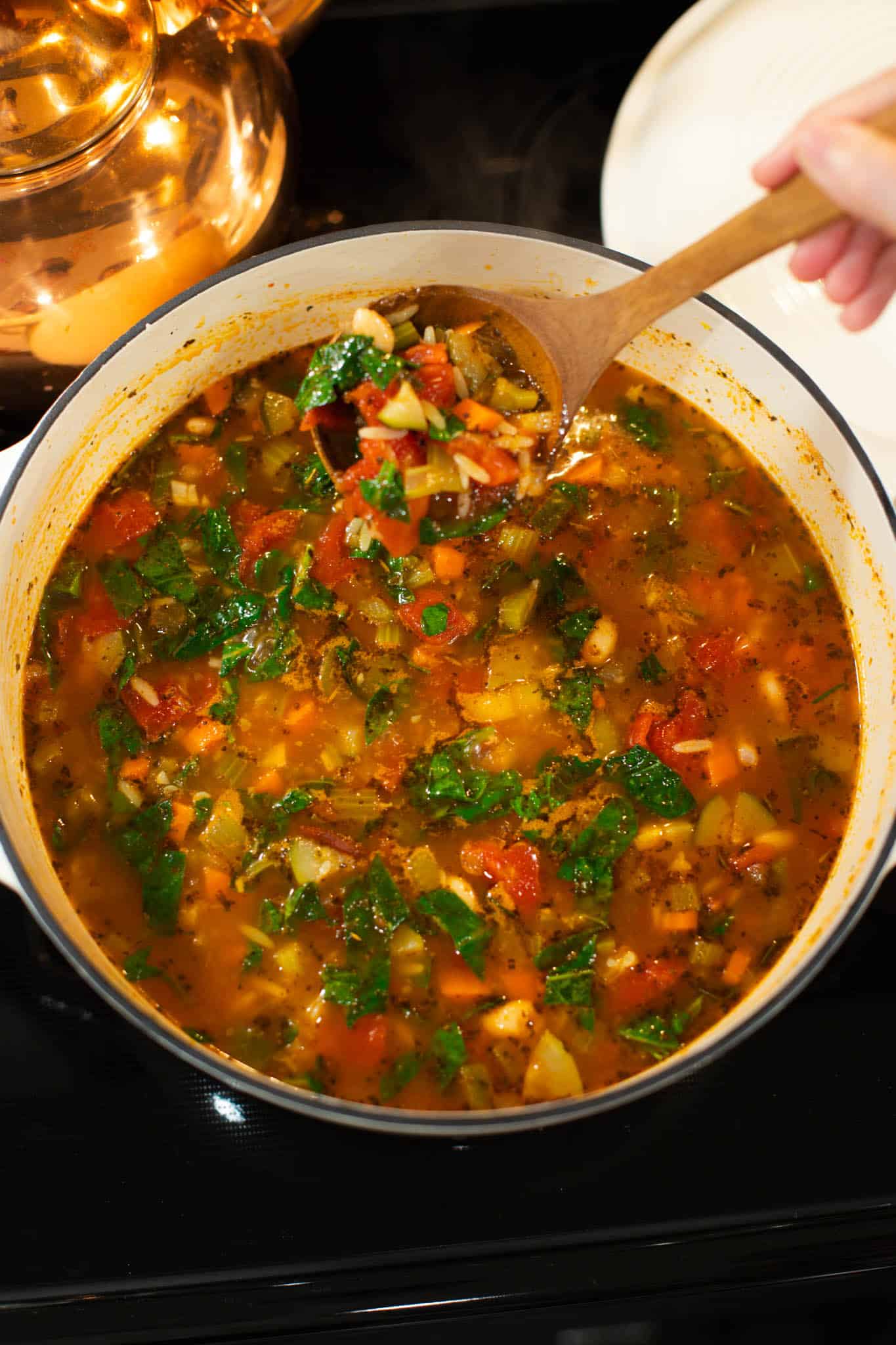 A close-up of the fully cooked minestrone soup, filled with colorful vegetables, beans, orzo, and spinach, ready to be served.
