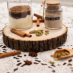 Homemade spiced chai latte mix in glass jars with cinnamon sticks and cardamom pods on wooden board