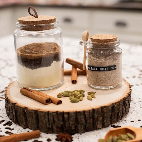 Homemade spiced chai latte mix in glass jars with cinnamon sticks and cardamom pods on wooden board