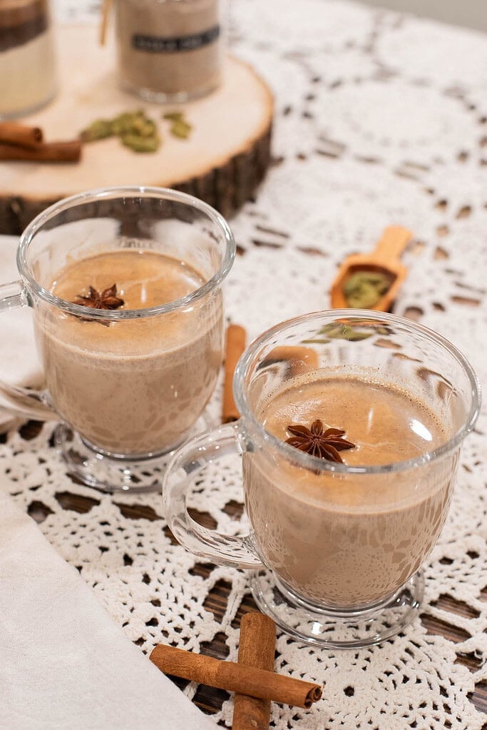 Homemade spiced chai latte in glass mugs topped with star anise on lace tablecloth