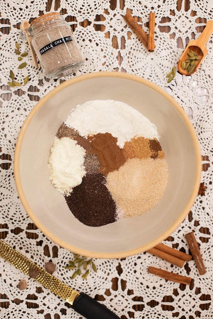 Dry ingredients for homemade chai latte mix in bowl with cinnamon sticks and ground spices