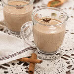 Another angle of two chai lattes, showing the frothy, spiced drink with star anise garnish, alongside scattered cinnamon sticks and cardamom pods for a rustic touch.