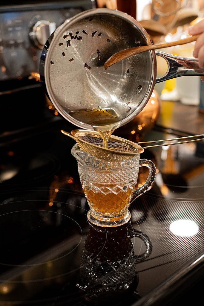 straining Earl Grey tea into glass mug for homemade London fog latte