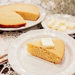 sourdough discard cornbread slice with butter on white plate with full cornbread in background