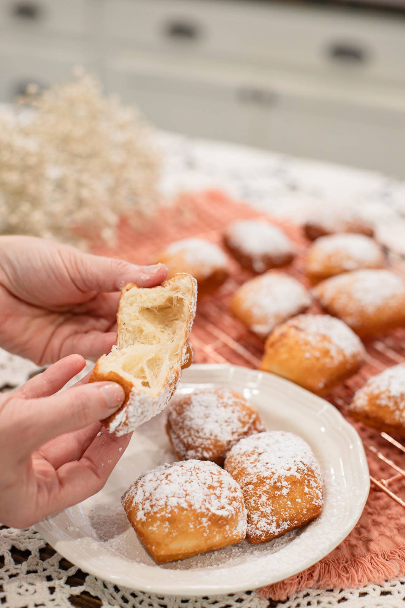 Hands pulling apart a sourdough beignet to show the light, airy interior crumb