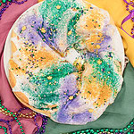 Sourdough king cake topped with white glaze and purple, green, and gold sanding sugar on a festive Mardi Gras table