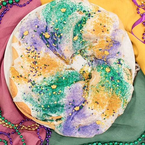 Sourdough king cake topped with white glaze and purple, green, and gold sanding sugar on a festive Mardi Gras table