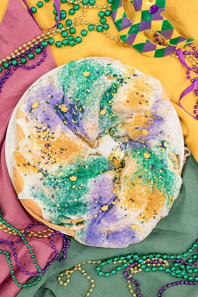 Sourdough king cake topped with white glaze and purple, green, and gold sanding sugar on a festive Mardi Gras table
