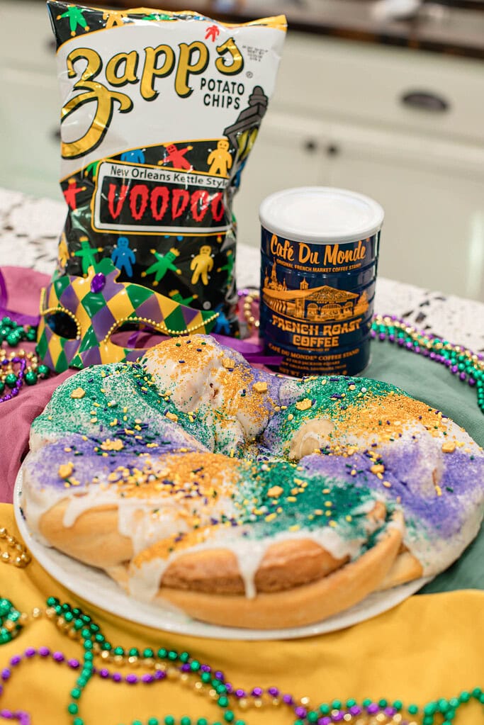 Glazed sourdough king cake decorated with Mardi Gras sugars alongside coffee and New Orleans–style snacks