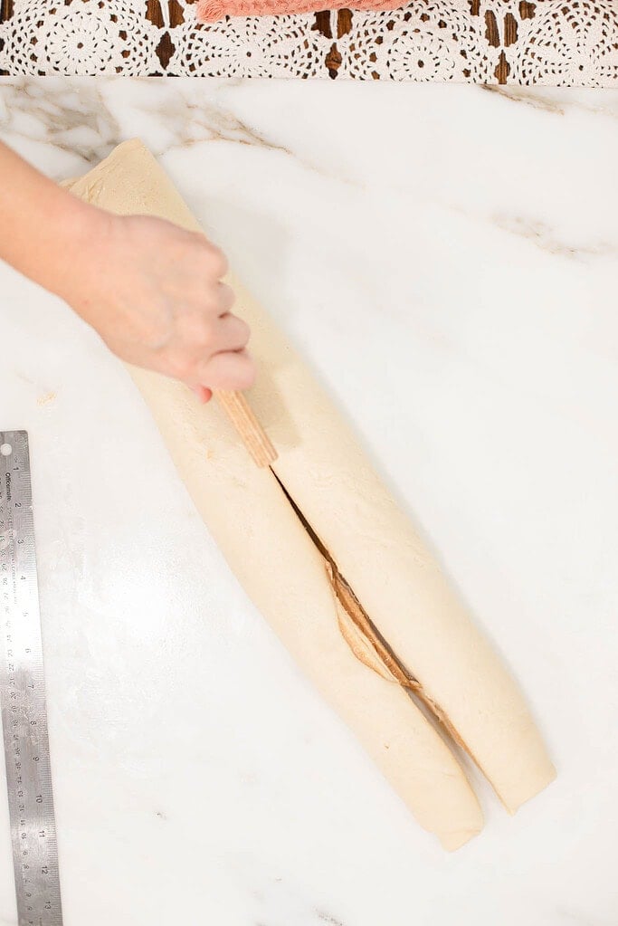 Rolled sourdough king cake dough log being sliced down the center to expose the cinnamon filling.