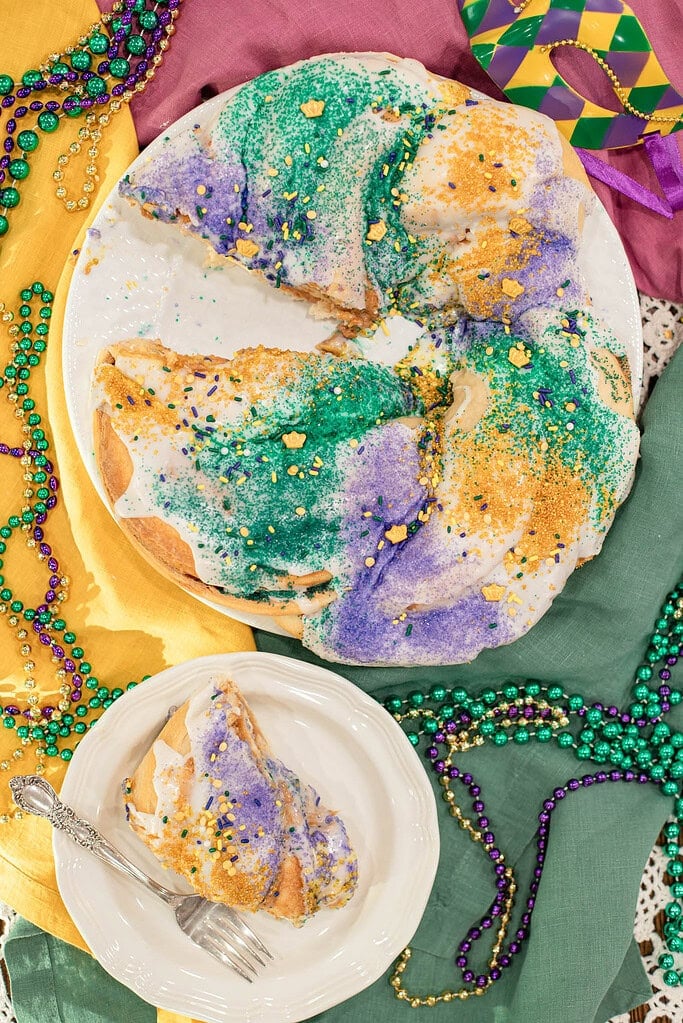 Sliced sourdough king cake showing soft interior and cinnamon filling under colorful Mardi Gras sugar topping
