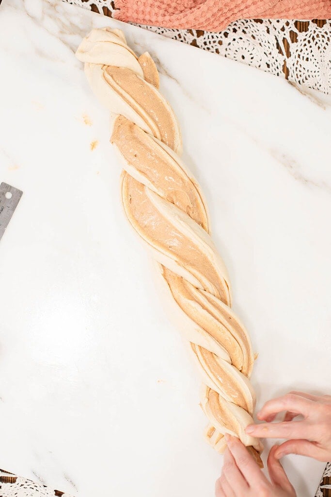 Braiding sourdough king cake dough with visible cinnamon filling swirled throughout.
