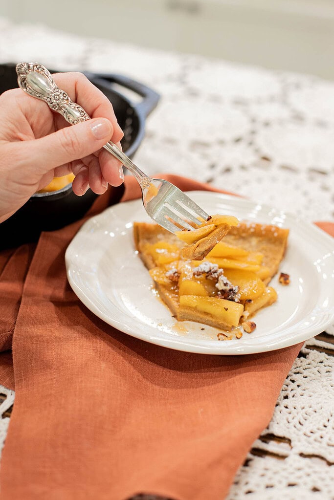 fork lifting bite of sourdough apple dutch baby pancake with caramel apples