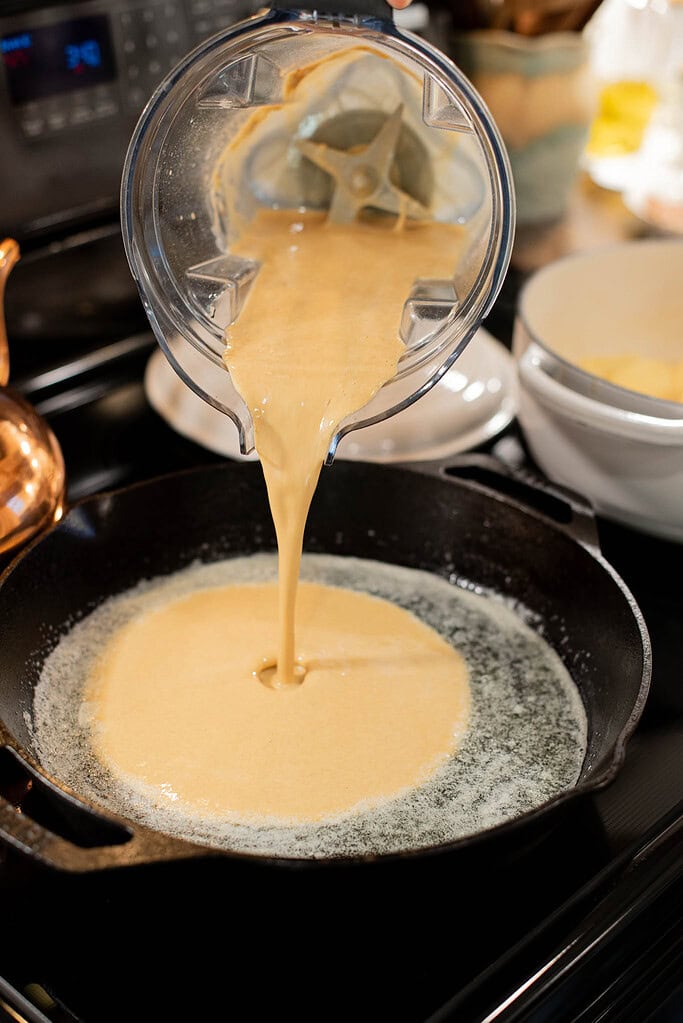 pouring sourdough dutch baby batter into hot cast iron skillet