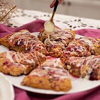 A hand lifting a glazed raspberry white chocolate sourdough scone from a plate, highlighting its texture and layers.