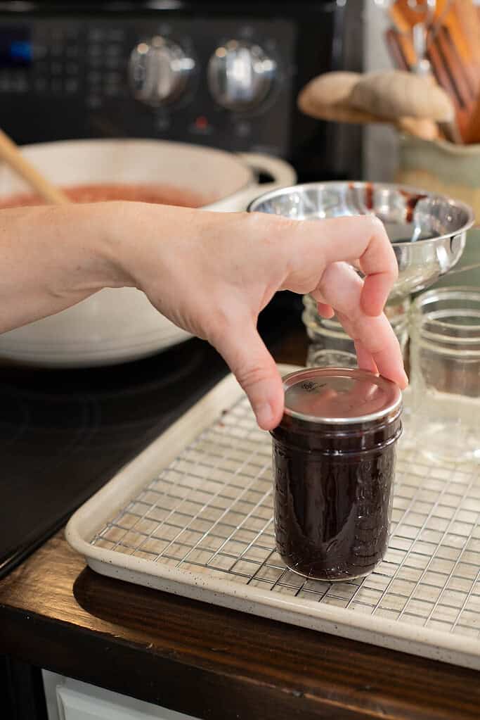 A person places a metal canning lid on the filled mason jar, ensuring a secure fit before processing.