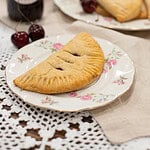 A close-up of a cherry hand pie, with a jar of cherry jam in the background, highlighting its golden crust.