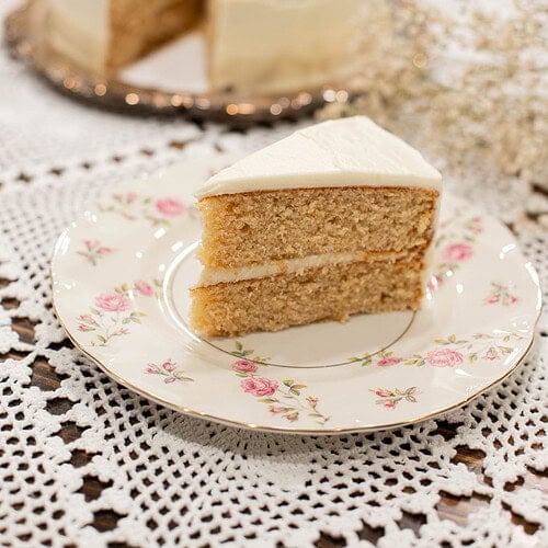 Slice of sourdough vanilla cake made with fresh milled flour on a floral vintage plate with white buttercream frosting and layered crumb visible.